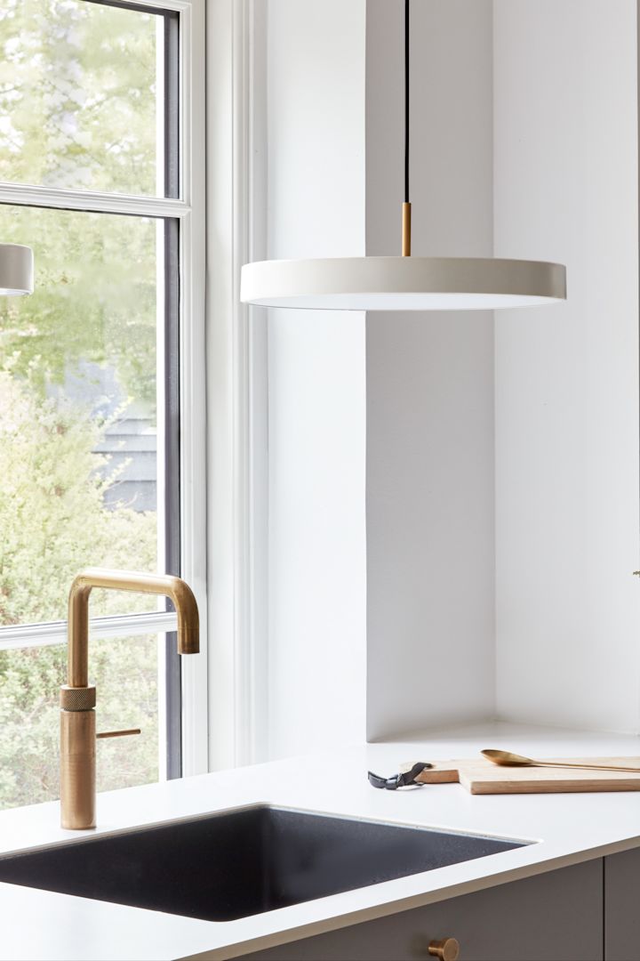Utiliza grandes lámparas colgantes si necesitas un poco más de luz en lugares como el fregadero. Aquí puedes ver la lámpara colgante Asteria Micro en perl blanco de Umage sobre un fregadero.