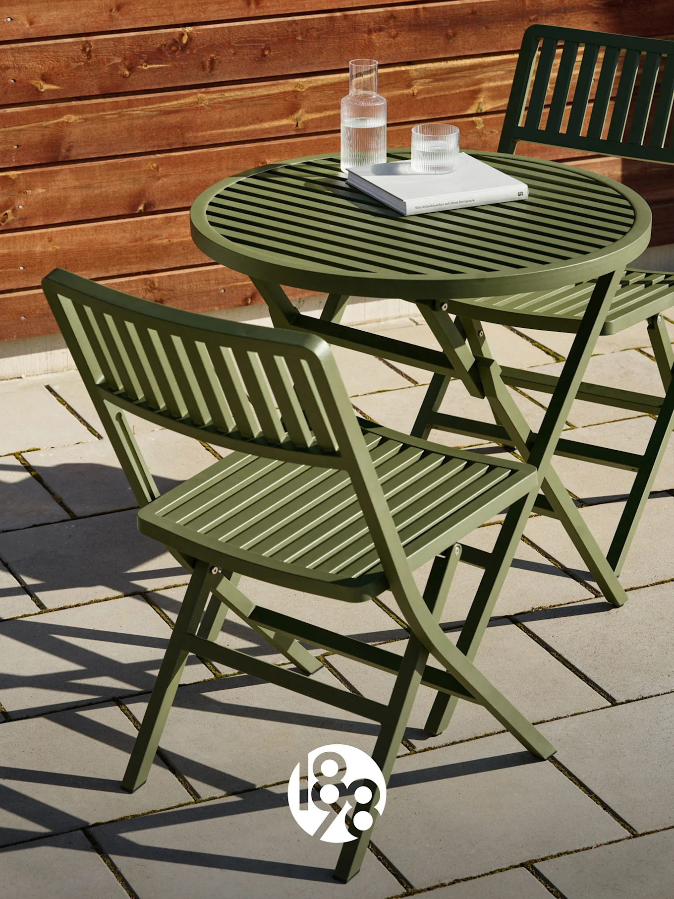 Dos sillas plegables verdes de lamas y una mesa a juego en un patio con un libro y vasos de agua.