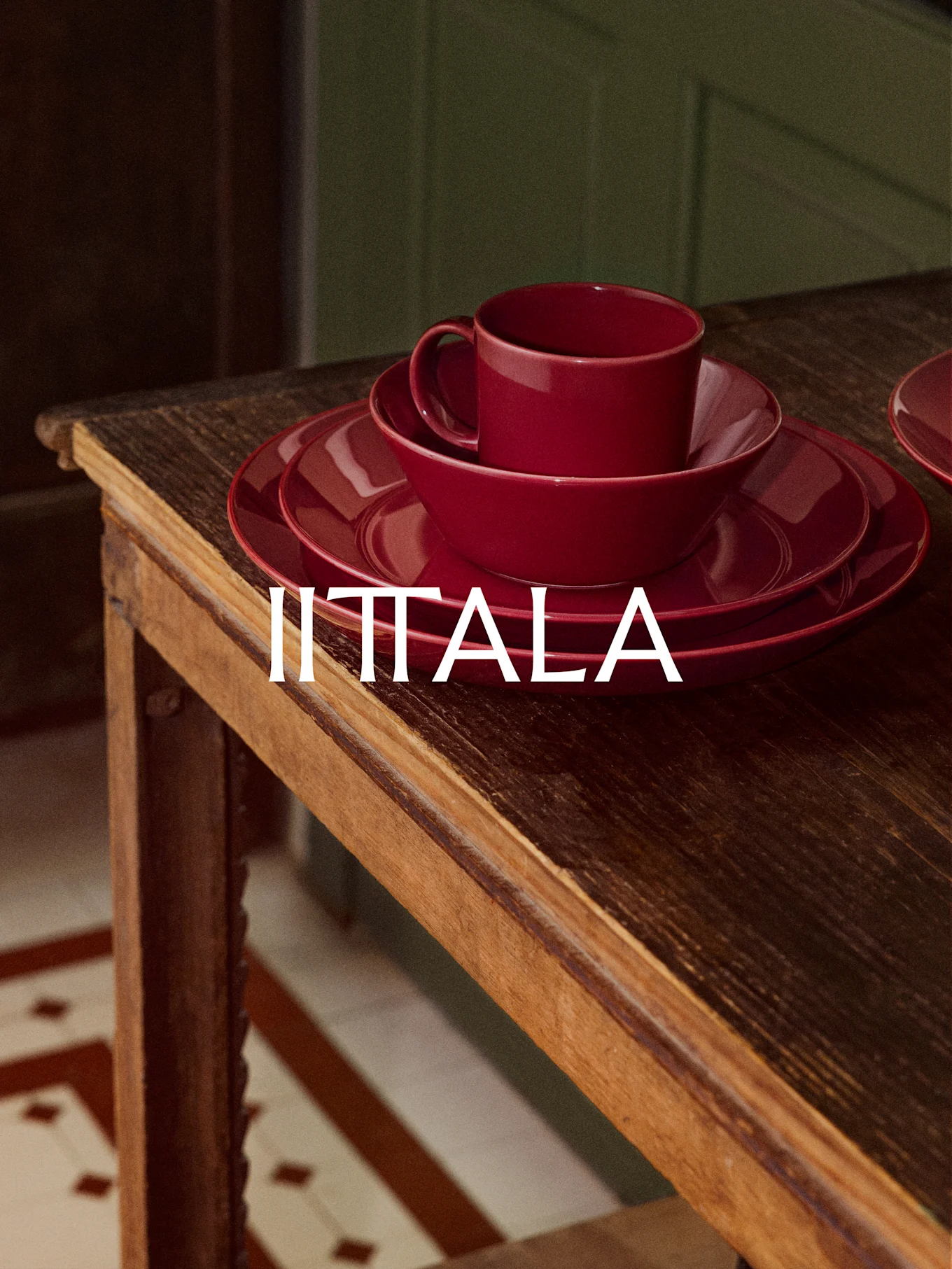 Una pila de vajilla roja IITTALA, que incluye una taza, un cuenco y platos, sobre una mesa de madera rústica.
