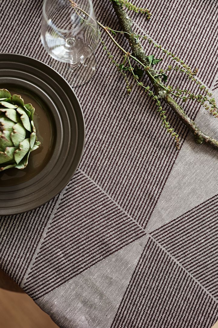 El mantel Geometric de NJRD en marrón con un plato de líneas marrones y una alcachofa verde. 