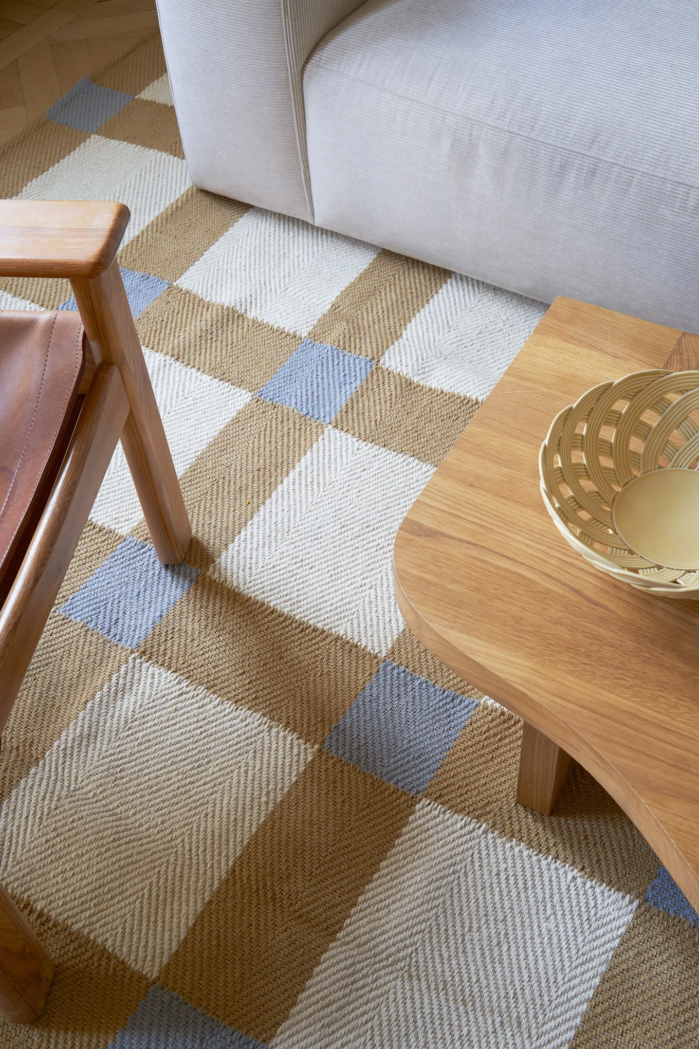 Vista aérea de una sala de estar con una alfombra con patrón de espiga blanca, marrón y azul claro, un sofá color crema y una mesa de centro de madera.