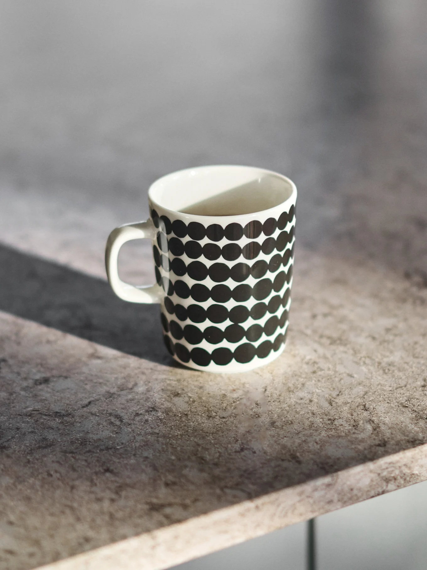 Taza de cerámica blanca con lunares negros sobre una encimera gris.