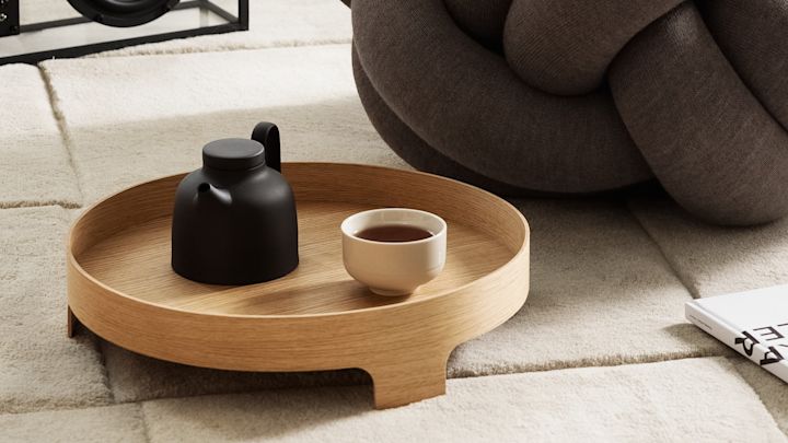 Lagom: La bandeja Bridge sobre una alfombra, con una tetera y una taza de té encima y el cojín XL al fondo, todo de Design House Stockholm.