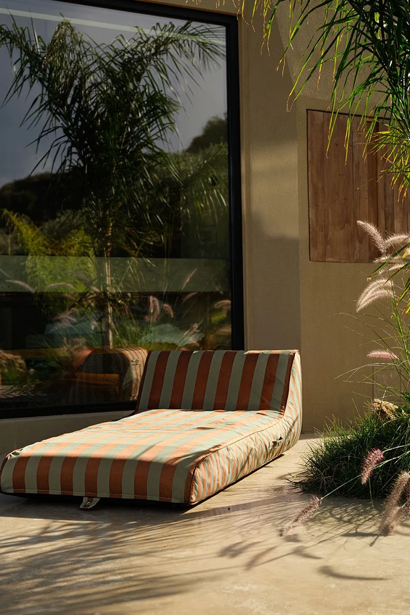 Tumbona a rayas en un patio con una gran ventana que refleja palmeras.