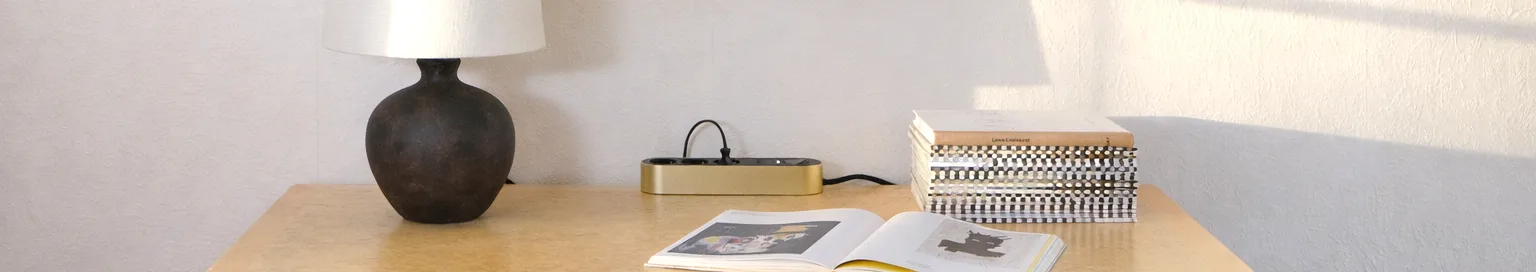 Regleta dorada con tres tomas de corriente negras y un botón de encendido sobre una superficie clara.