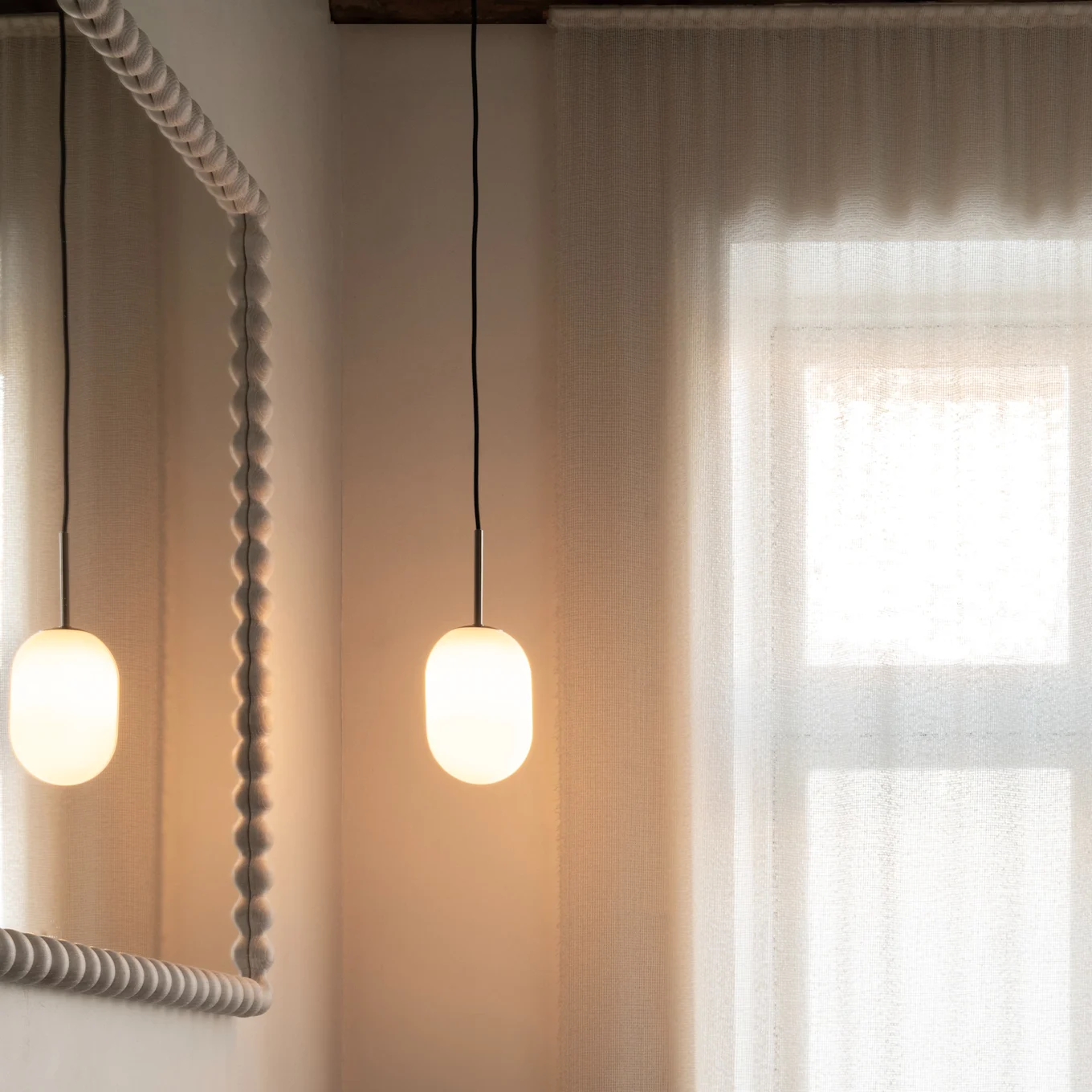 Baño moderno: tocador de madera, lavabo oscuro, grifo de bronce, espejo texturizado, lámparas colgantes, cortinas transparentes.