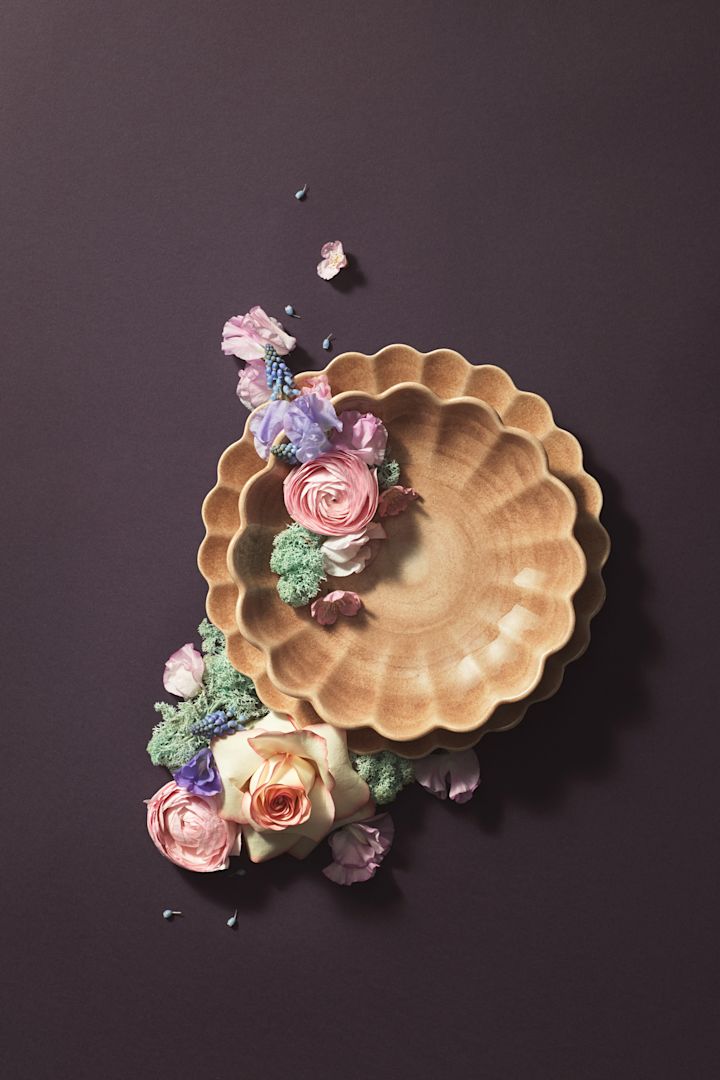 Un plato y un cuenco de la colección Oyster en color Cinnamon de Mateus han sido artísticamente escenificados con flores sobre un fondo marrón.