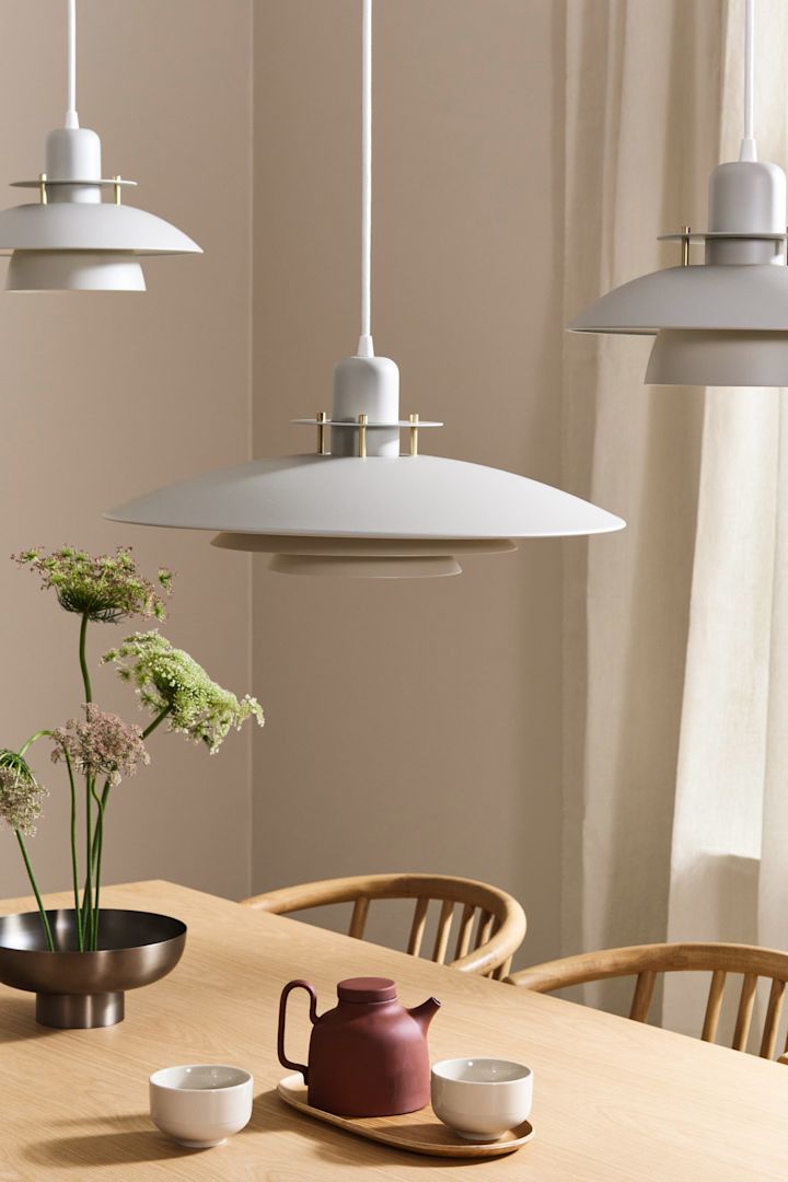 Tres lámparas blancas Priums de Belid colgadas sobre una mesa de comedor de roble de estilo Japandi.
