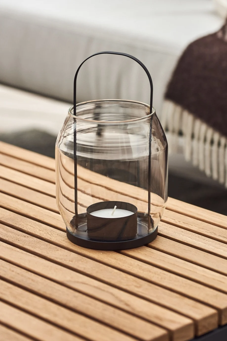 Faroles y portavelas para exteriores: aquí puede ver un farol ERNST de cristal y metal negro sobre una mesa de madera de balcón.