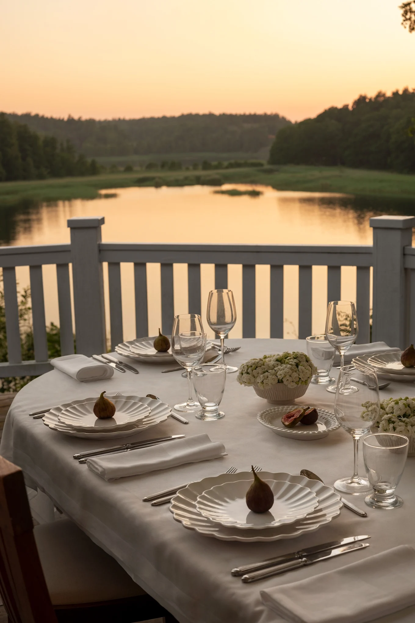 Una mesa al atardecer en una terraza con vistas a un lago. La mesa está puesta en blanco con platos de la colección Oyster de Mateus.