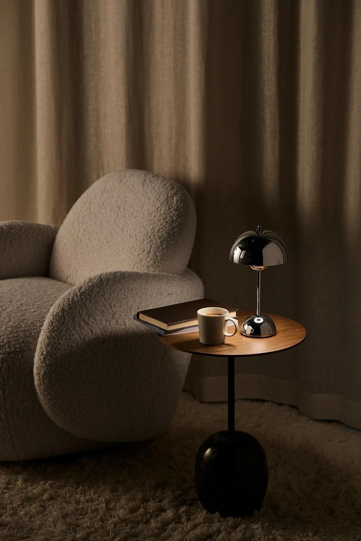 Junto al sillón Mo de 1898 hay una mesa de centro con un libro, una taza de café y la lámpara de mesa Flowerpot en color cromado de &Tradition.