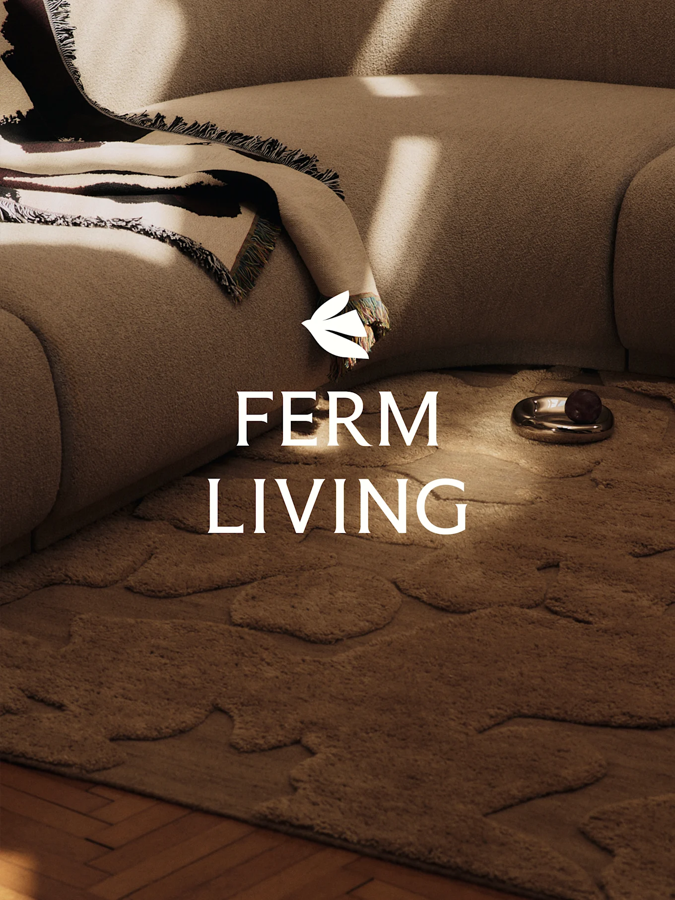 Una escena acogedora con un sofá texturizado marrón claro, una manta estampada, una alfombra marrón con formas orgánicas y un plato decorativo.