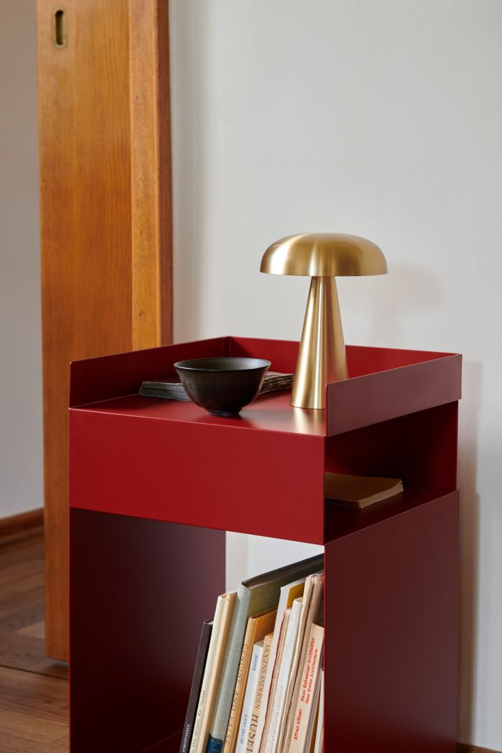 Los muebles y detalles interiores en rojo son una gran tendencia en el diseño de interiores escandinavo para 2024, y se pueden ver aquí en &Tradition en forma de una mesa auxiliar roja con una pequeña lámpara de latón sobre ella.