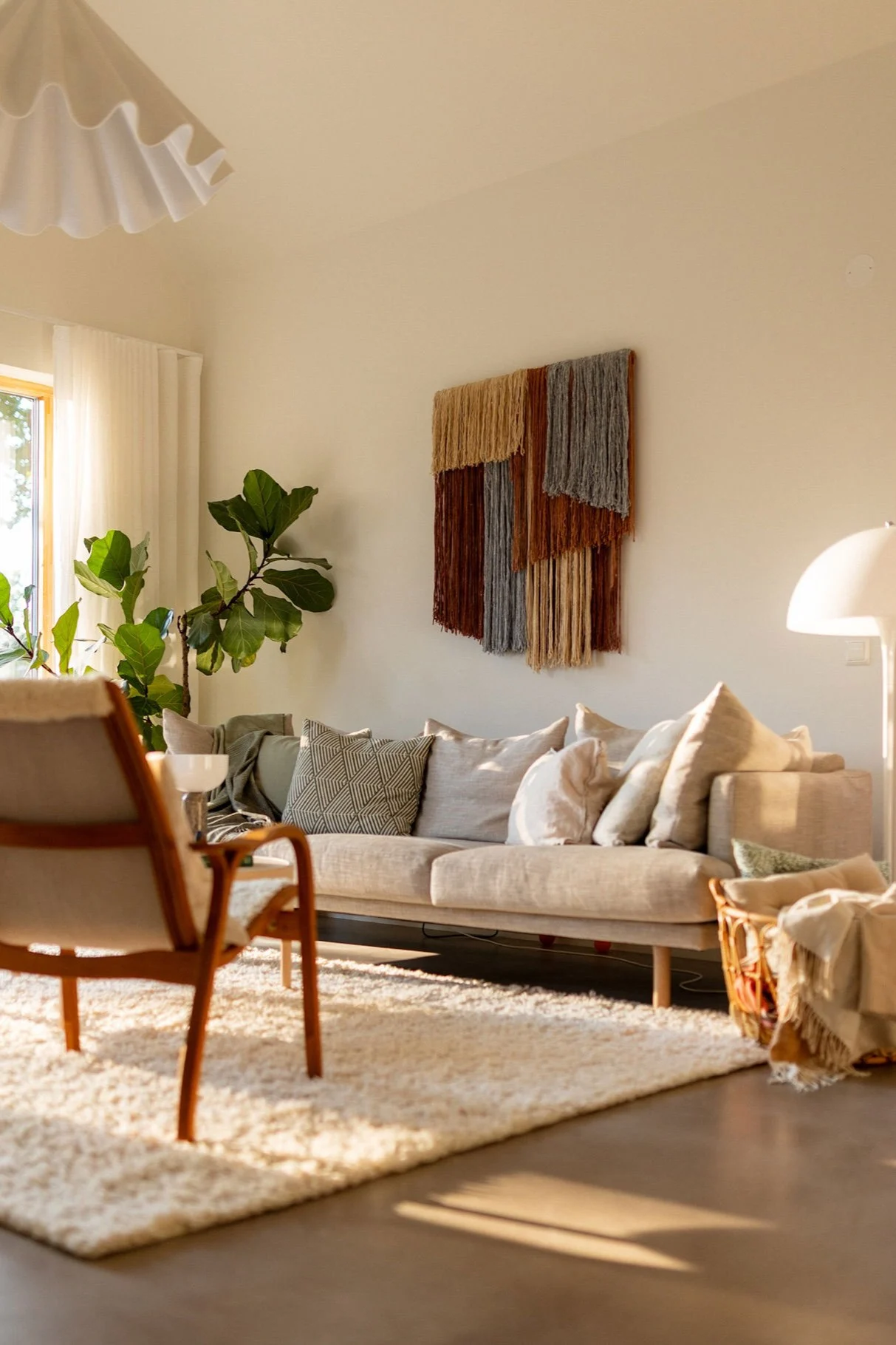 La decoración mural textil de Tham, de Tinted, cuelga de la pared de un salón, sobre un sofá. 