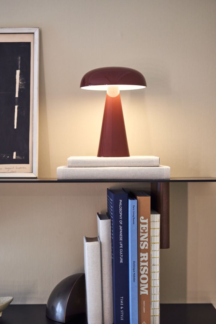 La lámpara de mesa inalámbrica Como de &Tradition colocada en un estante junto a libros y un marco de fotos.