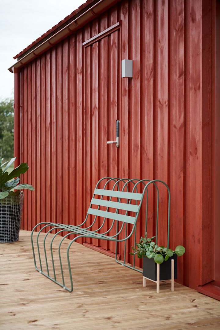 Tendencias en muebles de jardín 2025: el sofá Gardeners de Design House Stockholm, en color verde, se coloca en una terraza frente a una casa sueca roja de madera.