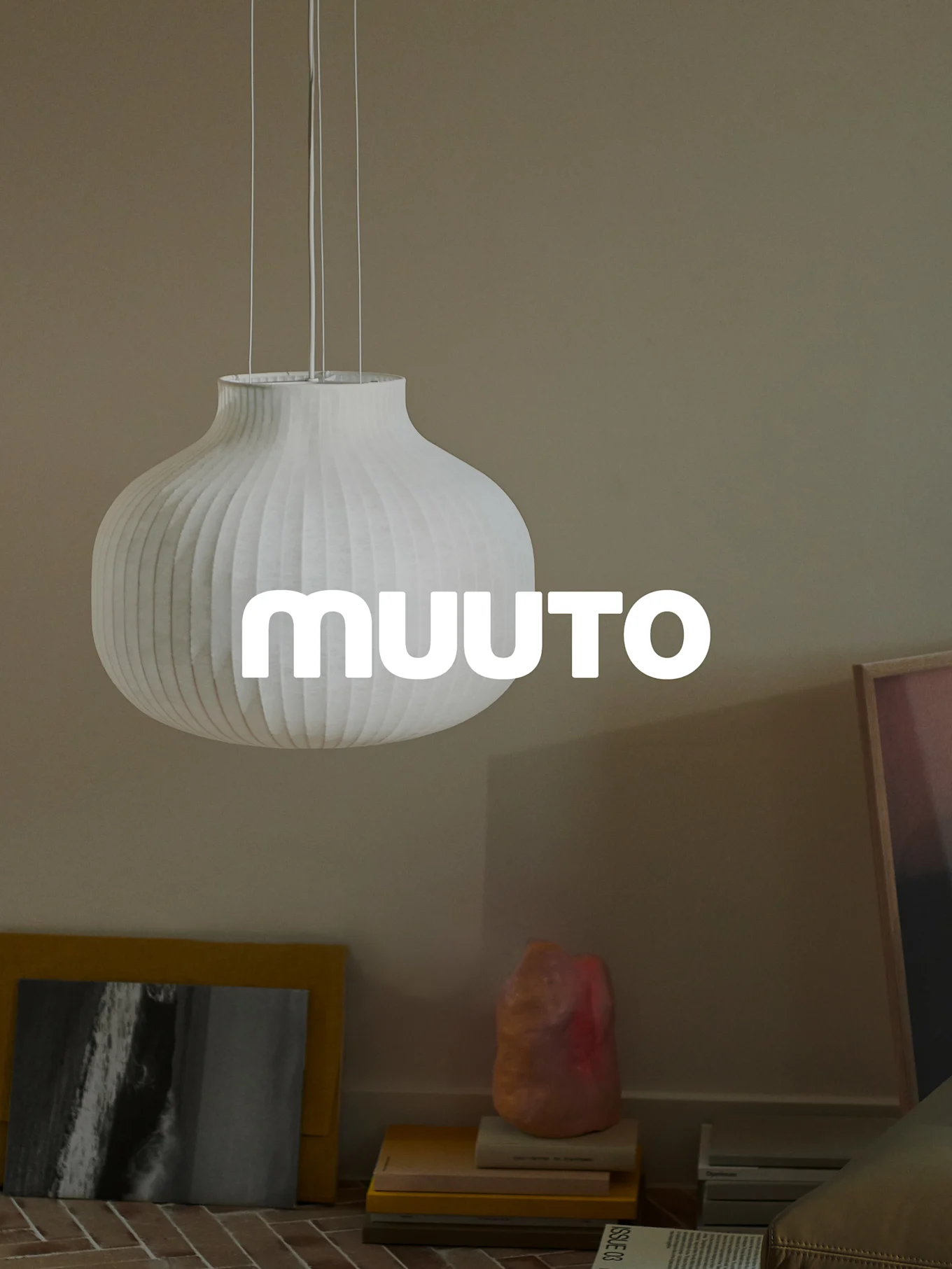 Lámpara colgante blanca acanalada con forma de calabaza con el logo 'MUUUTO', en una habitación beige.