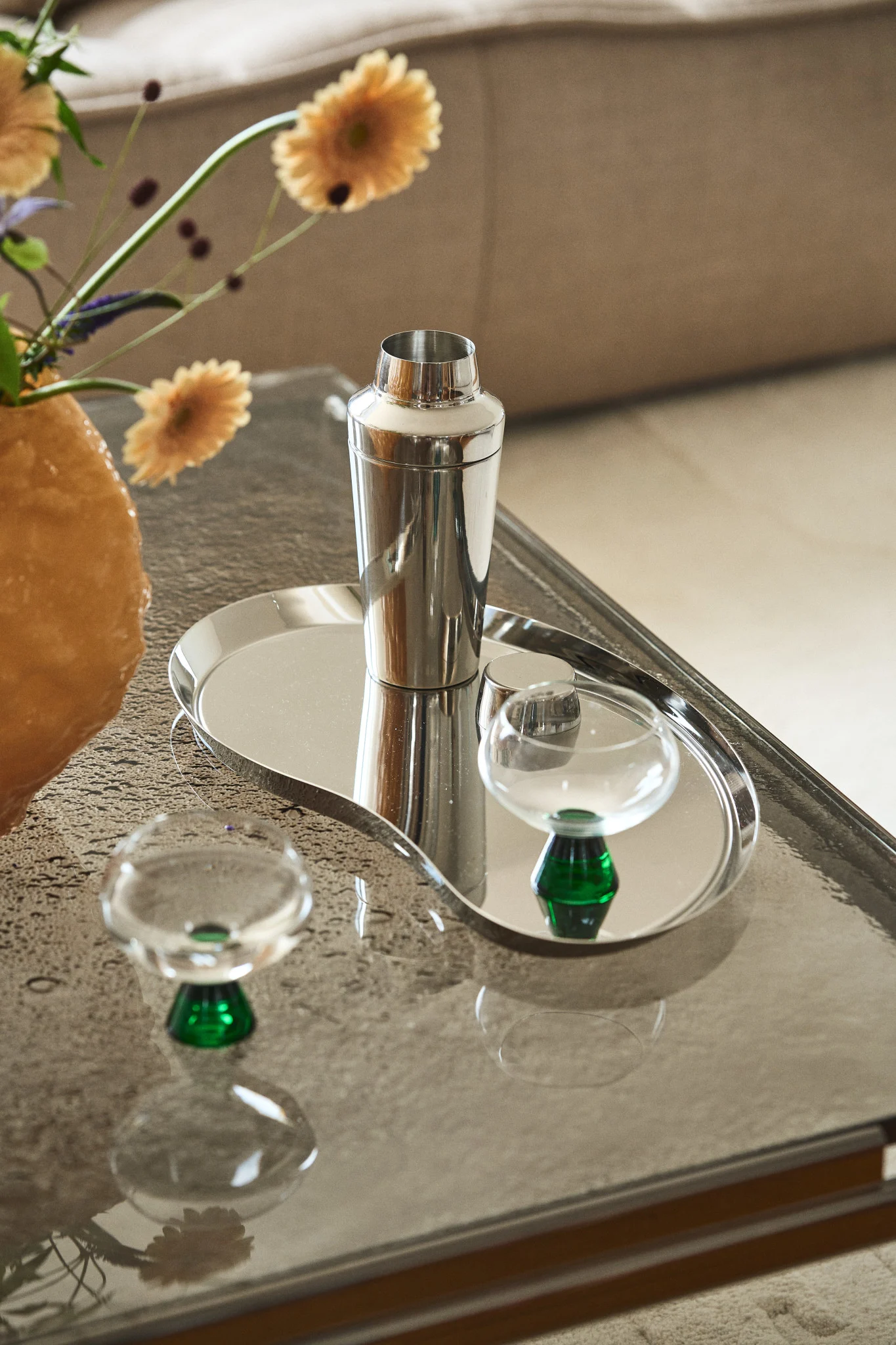 Regala un set de cócteles o bonitas copas para el Día de San Valentín. Aquí se muestra el shaker Grand Cru de Rosendahl sobre una bandeja de color cromo en una mesa de centro, junto a las copas Indy de Byon.