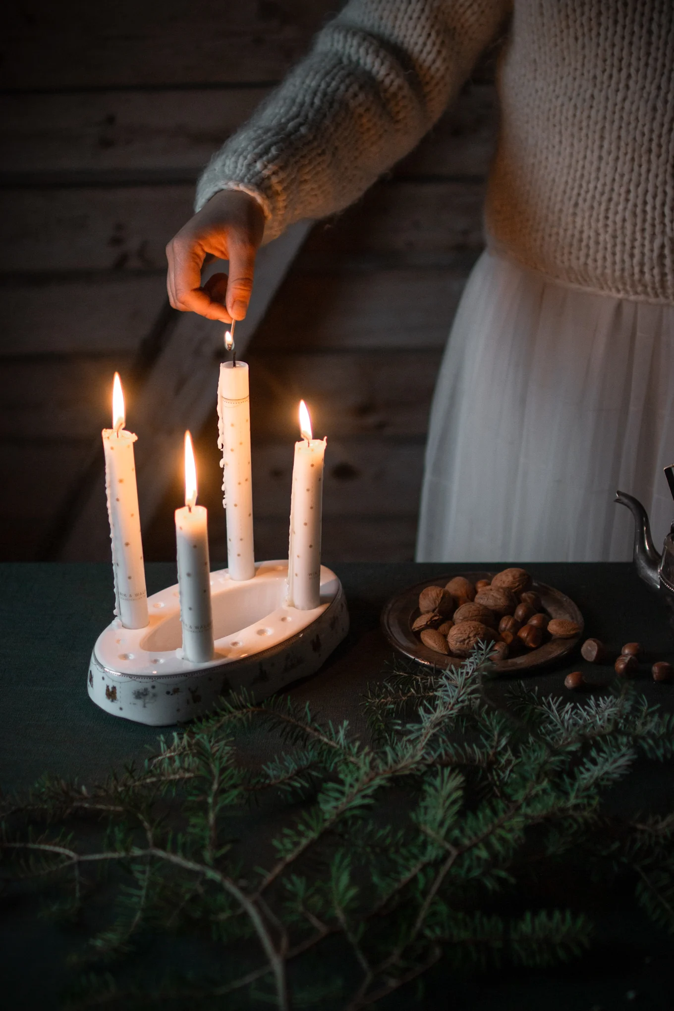 El portavelas Julemorgen Story de Wik & Walsøe está sobre una mesa decorada con ramas de abeto en un ambiente navideño.