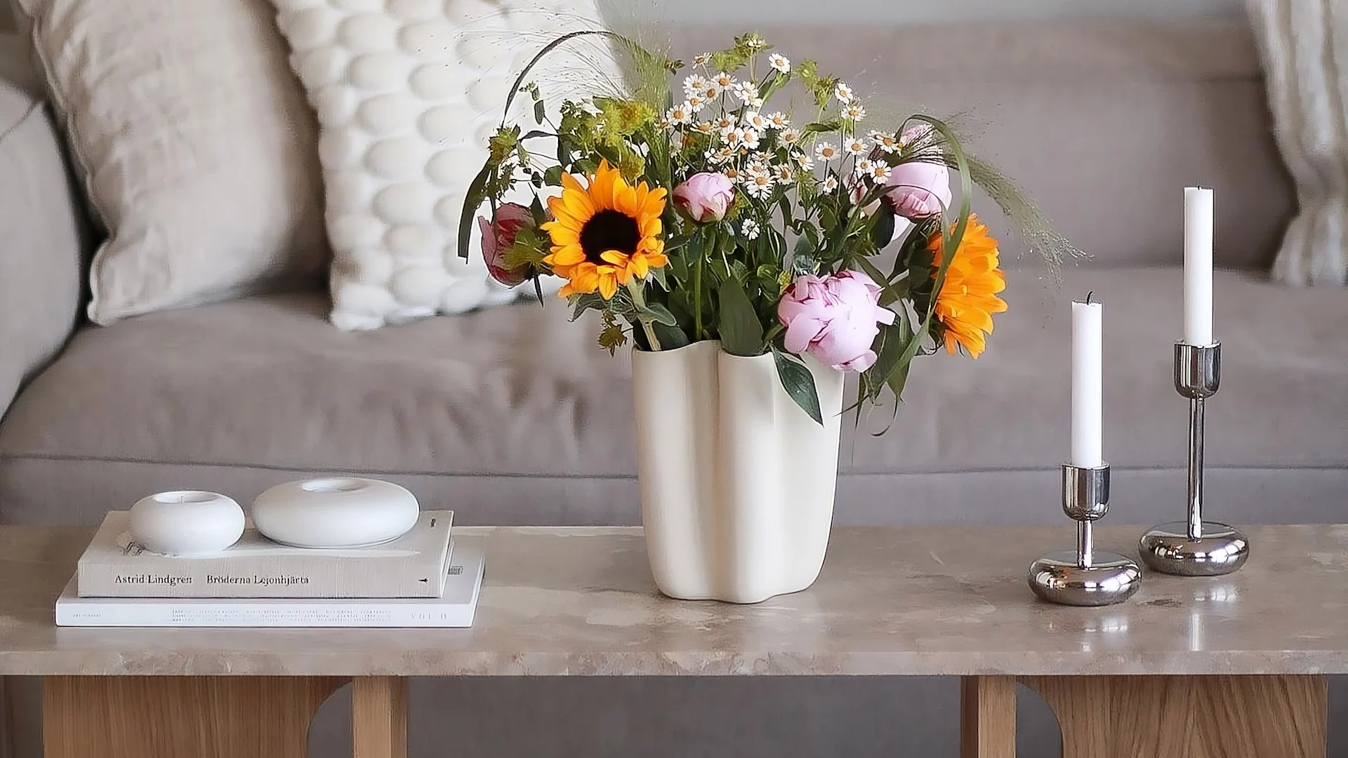 La mesa de lounge Androgyne de Audo Copenhagen está decorada con flores frescas, dos candelabros Nappula de Iittala y los portavelas Stone de Scandi Living.