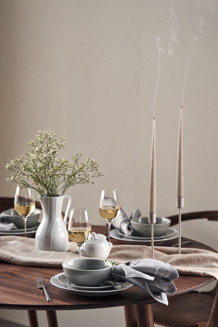 Una mesa de evento con velas, flores silvestres en una jarra de Pli Blanc y porcelana Swedish Grace en blanco y gris. 