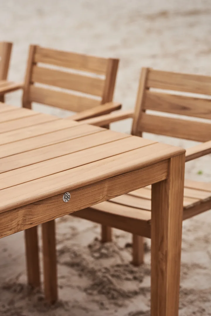 Mesa de comedor de madera para exterior con sillas en la arena, con una placa '188'.