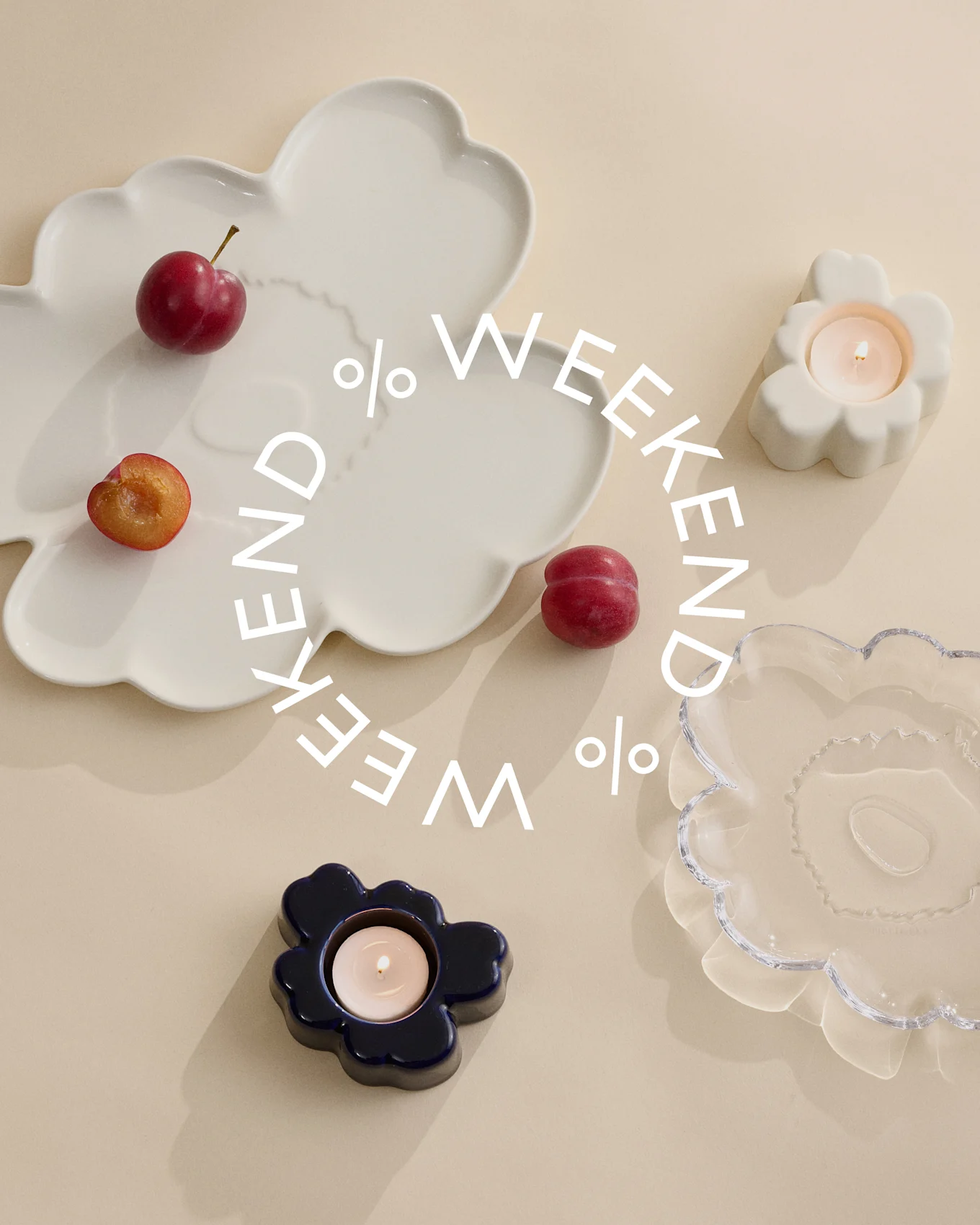 Platos decorativos y portavelas en blanco, azul y cristal transparente con ciruelas sobre fondo beige. Texto blanco dice 'Weekend %'.