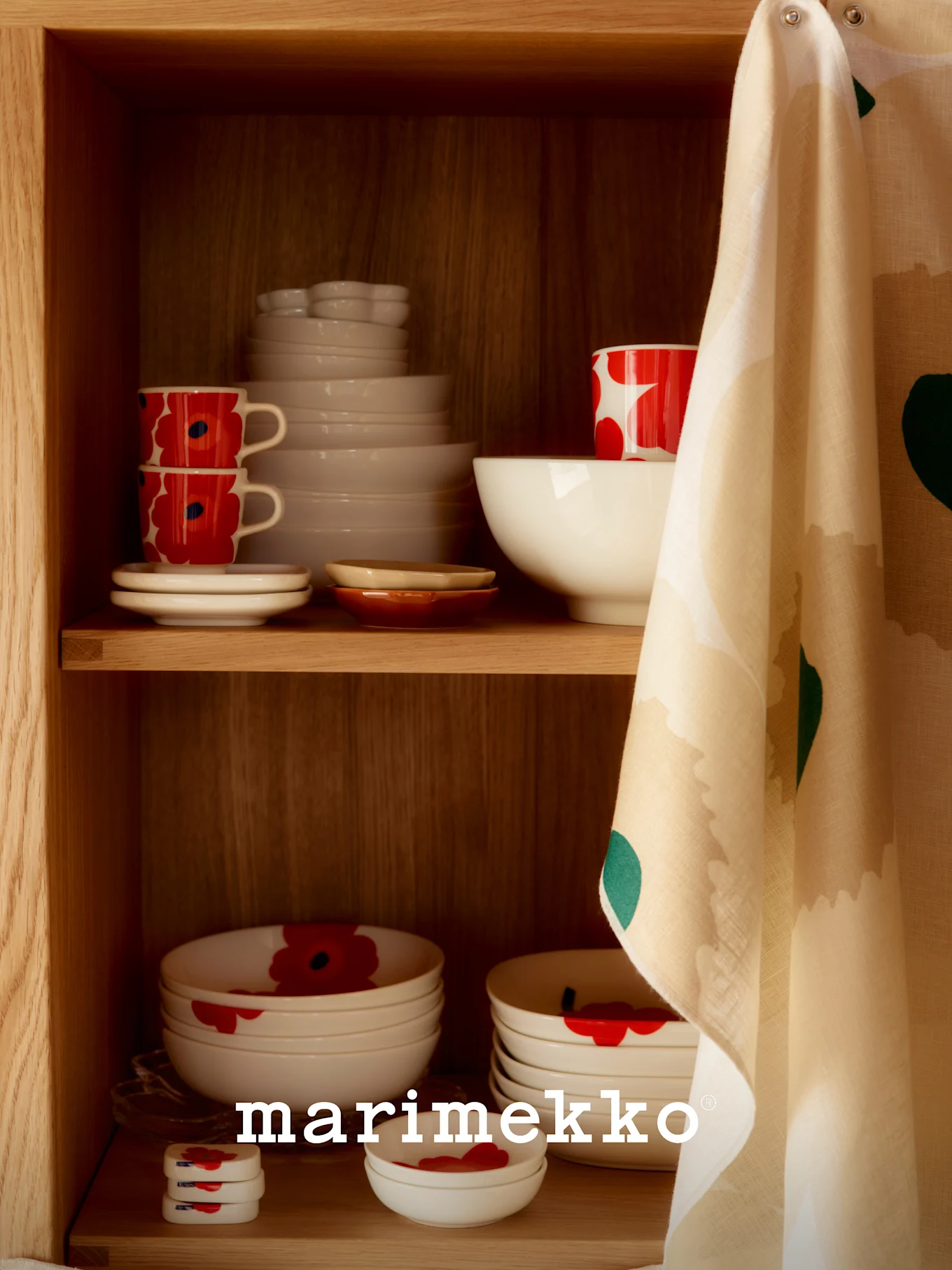 Una estantería de madera con vajilla de cerámica blanca, algunas con un patrón de amapolas rojas, y un paño de cocina estampado colgado a un lado.
