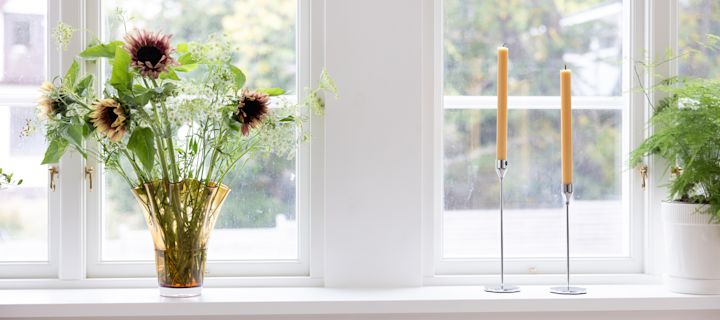 Dale un toque primaveral a tu ventana con una decoración sencilla pero elegante. Utiliza el jarrón Viva en color ámbar para realzar la belleza de tus flores frescas y combínalo con los portavelas Siri en diferentes tamaños para crear un ambiente cálido y acogedor.
