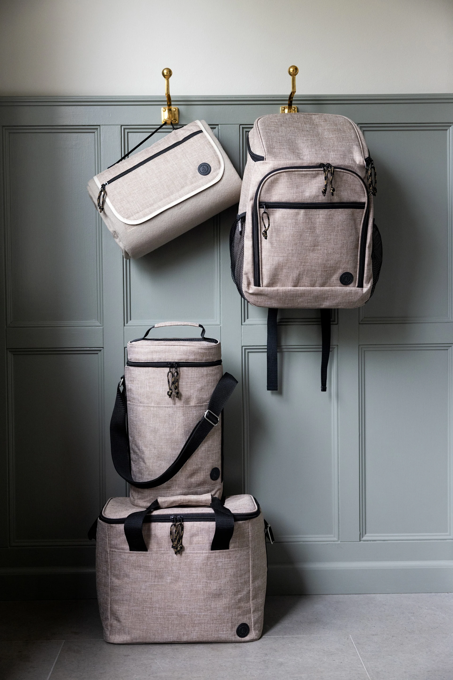 Cuatro bolsas beige claro: una bolsa plana y una mochila cuelgan de ganchos, una nevera cilíndrica y una rectangular apiladas debajo.