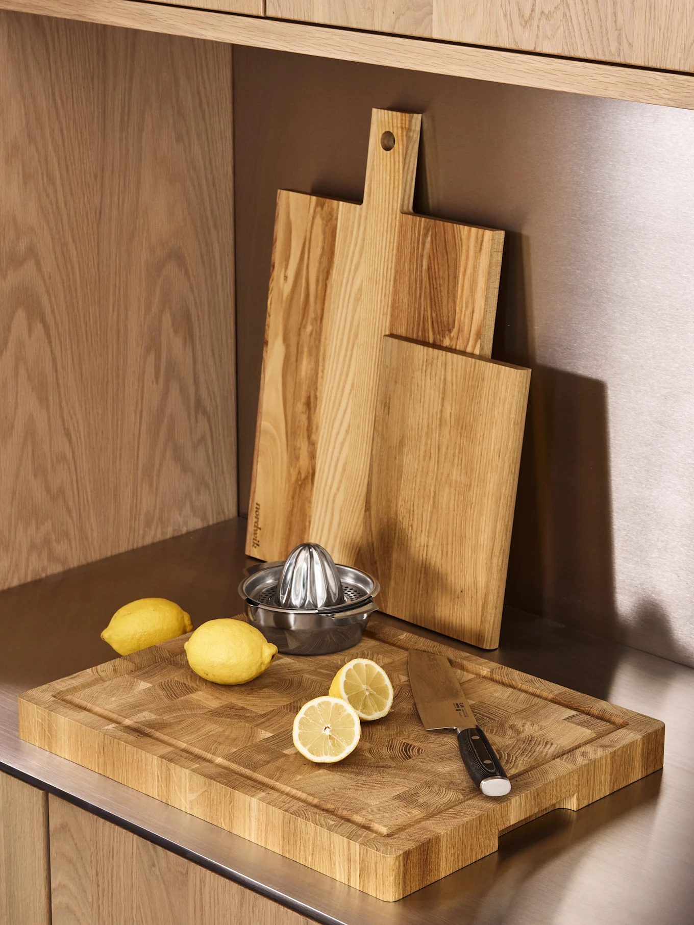 Tres tablas de cortar de madera, un exprimidor de limones de acero inoxidable y limones frescos en una encimera de cocina.