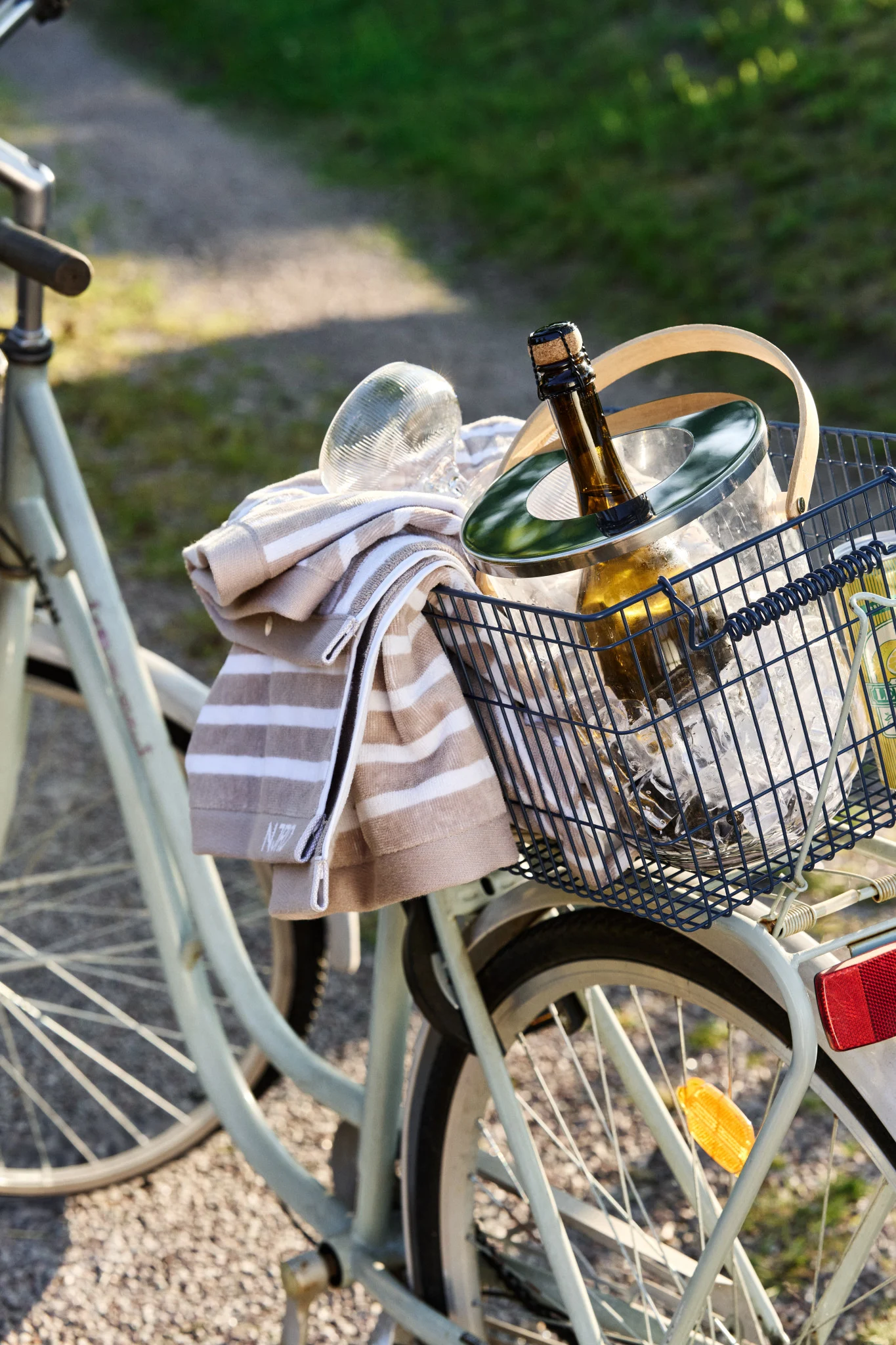 Una cesta de bicicleta contiene una cubitera con una botella fría y una toalla a rayas en un día soleado.