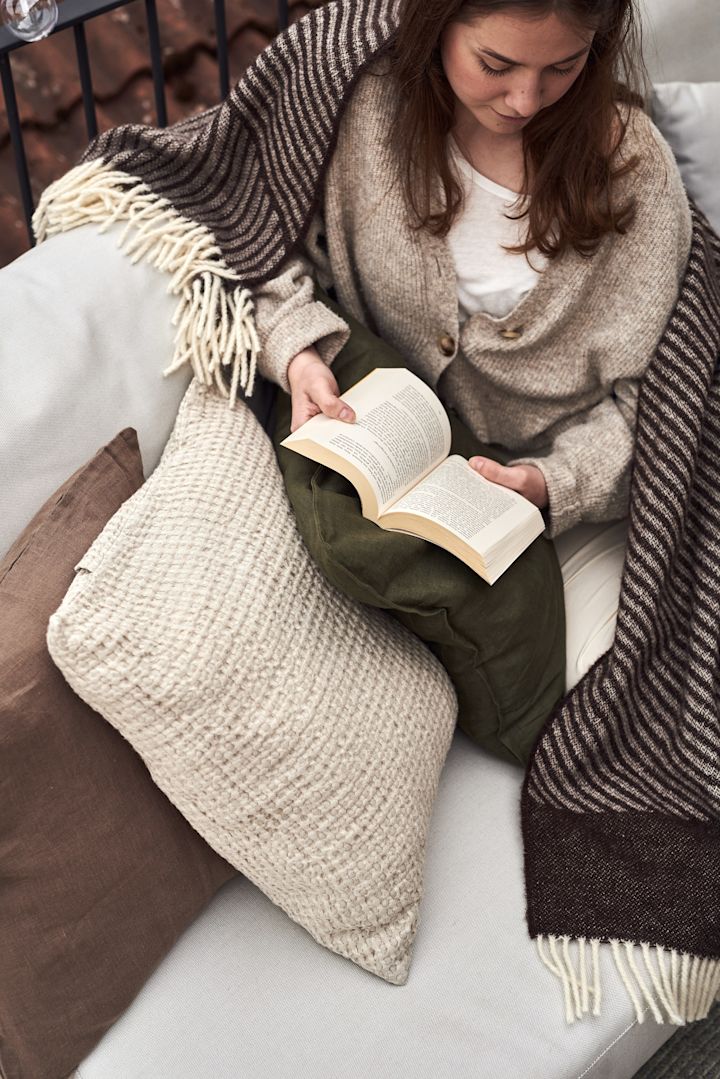 Una mujer está sentada en un sofá del balcón leyendo un libro.