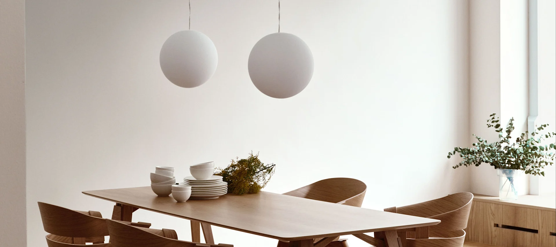 La lámpara Luna de Design House Stockholm colgada en pareja sobre una mesa de comedor de madera.
