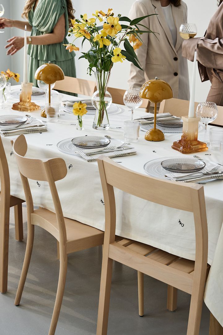 Una mesa de fiesta con toques amarillos e invitados socializando alrededor. Aquí ves la lámpara Flowerpot VP9 de Tradition con el candelabro Rocky Baroque en ámbar.
