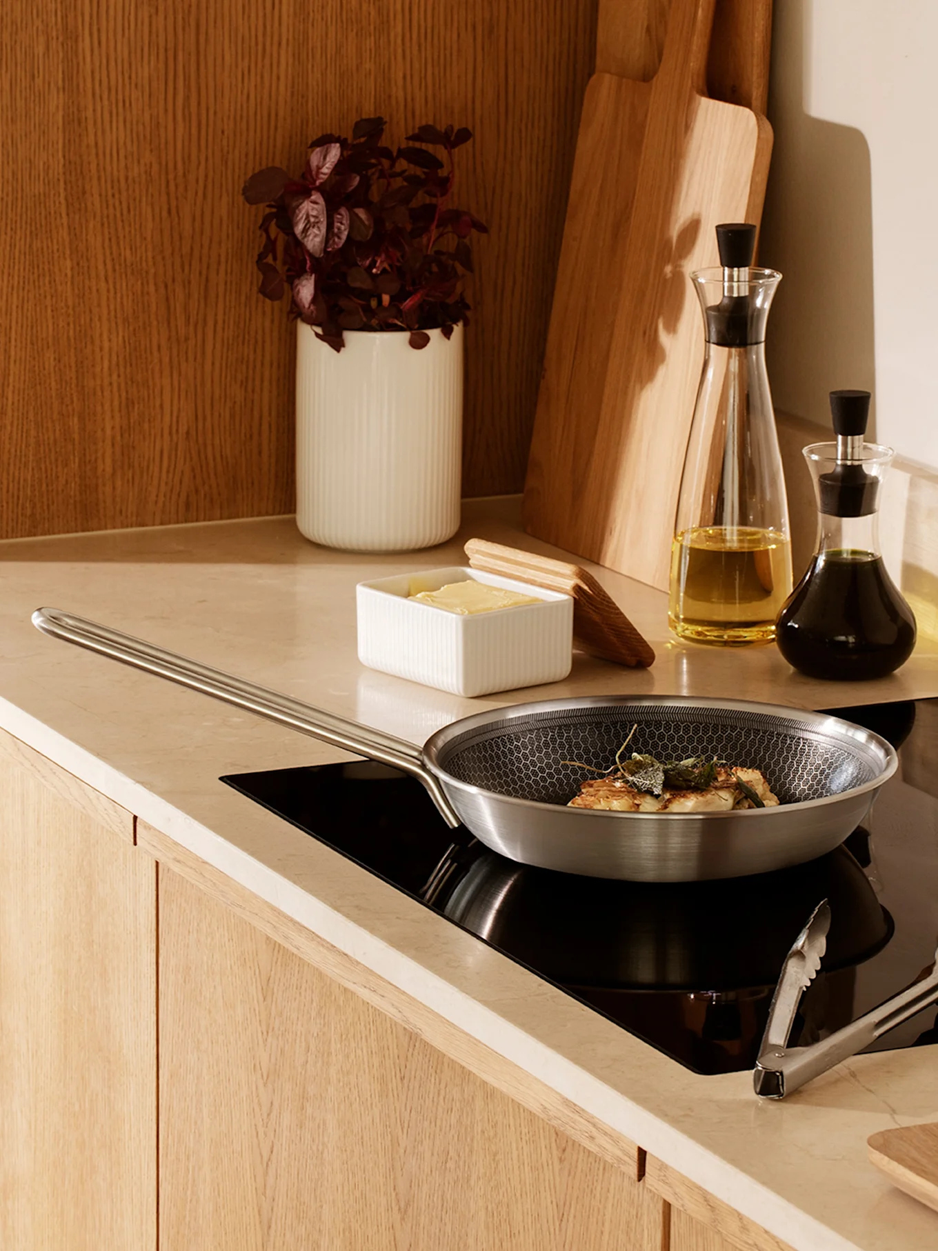 Una sartén de acero inoxidable con patrón de panal cocinando comida con salvia en una placa de inducción negra en una cocina moderna.