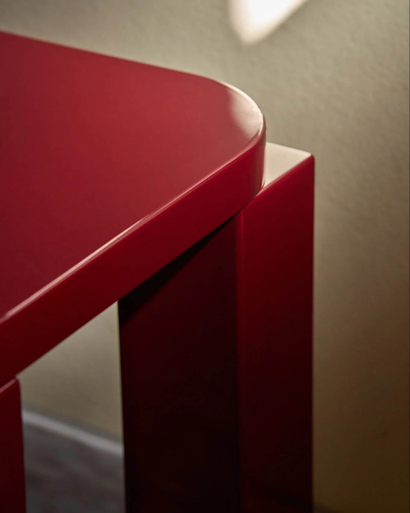 Un taburete rojo brillante con tapa rectangular redondeada, sobre un suelo de baldosas junto a una pared con azulejos rojos.