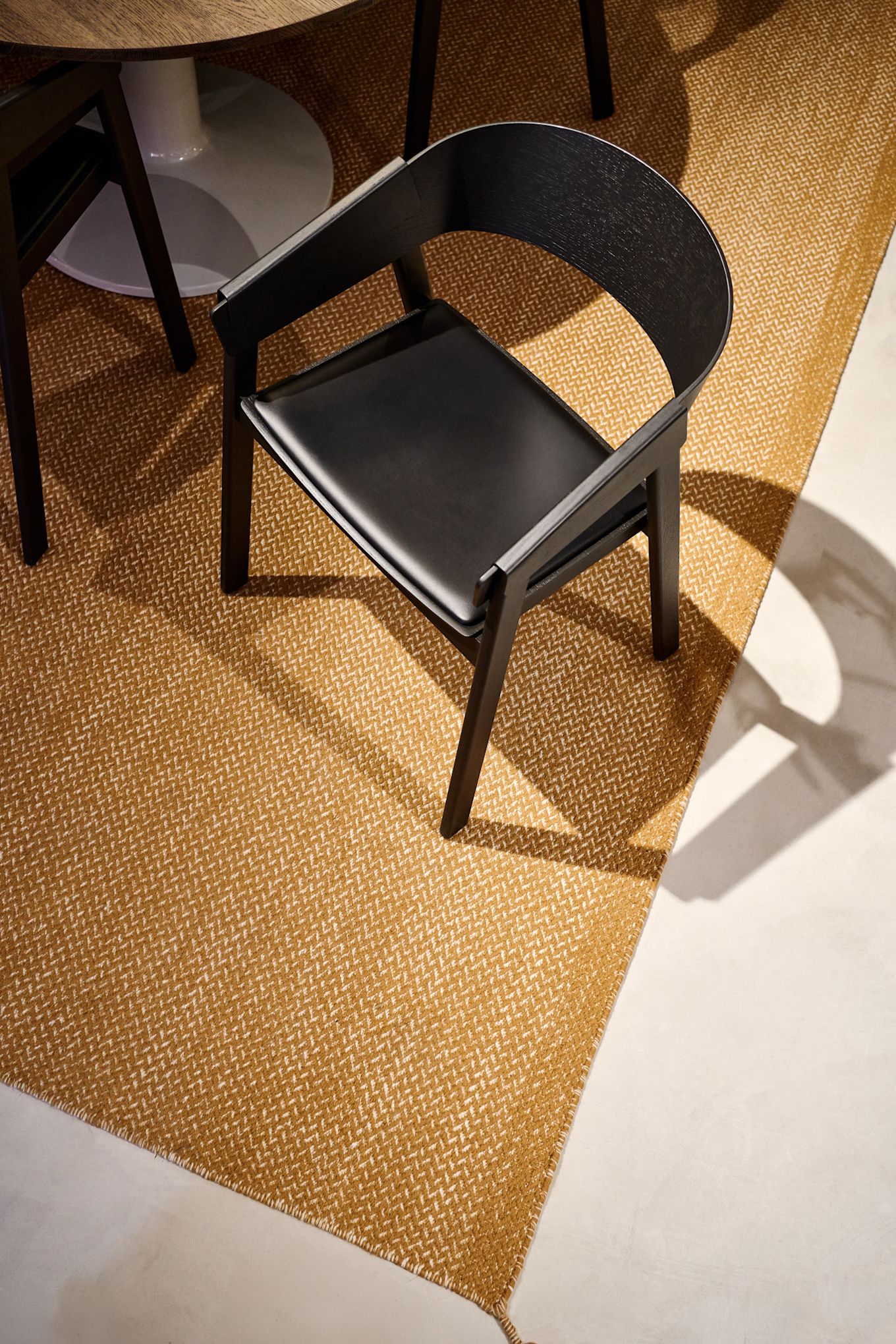 El sillón Cover negro con asiento de cuero de Muuto sobre una alfombra color mostaza.