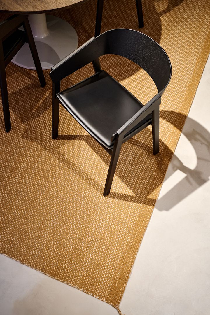 El sillón Cover negro con asiento de cuero de Muuto sobre una alfombra color mostaza.