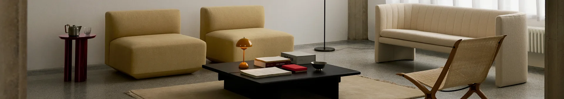 Una sala de estar moderna con dos sillas mostaza sin brazos, una mesa de centro negra, un sofá acanalado crema y una silla de madera tejida.