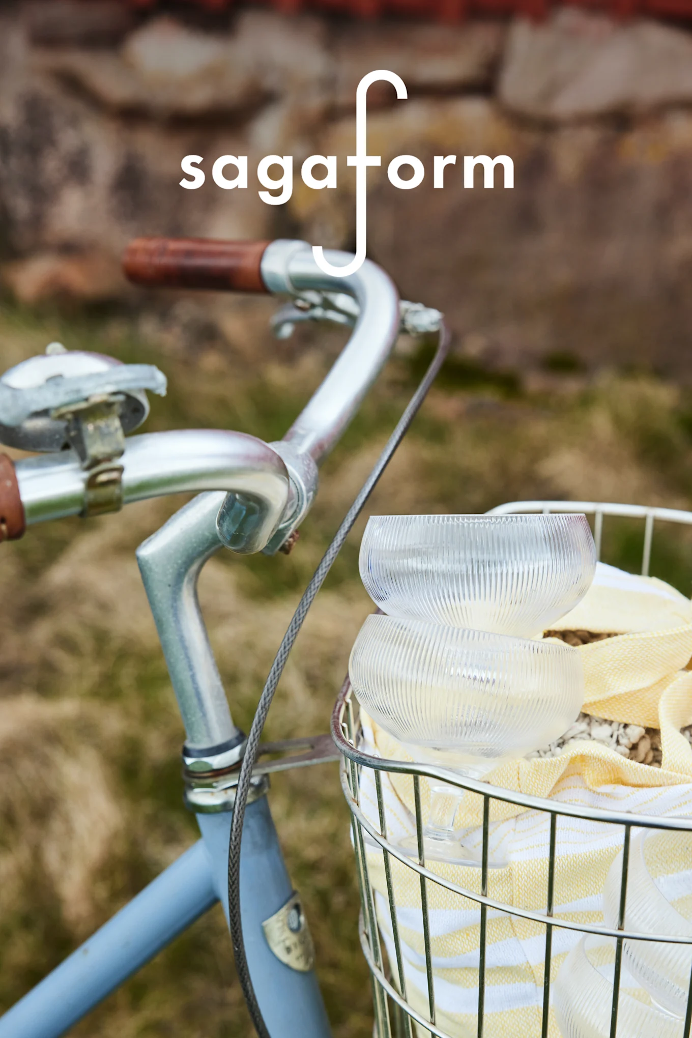 Dos cuencos de vidrio transparentes y acanalados y una toalla a rayas amarillas en una cesta de bicicleta. Logotipo de 'sagaform'.