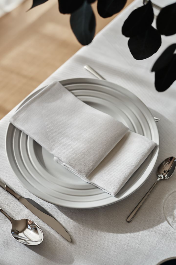Una mesa blanca y nítida con una servilleta blanca doblada y un mantel blanco y porcelana blanca de NJRD.