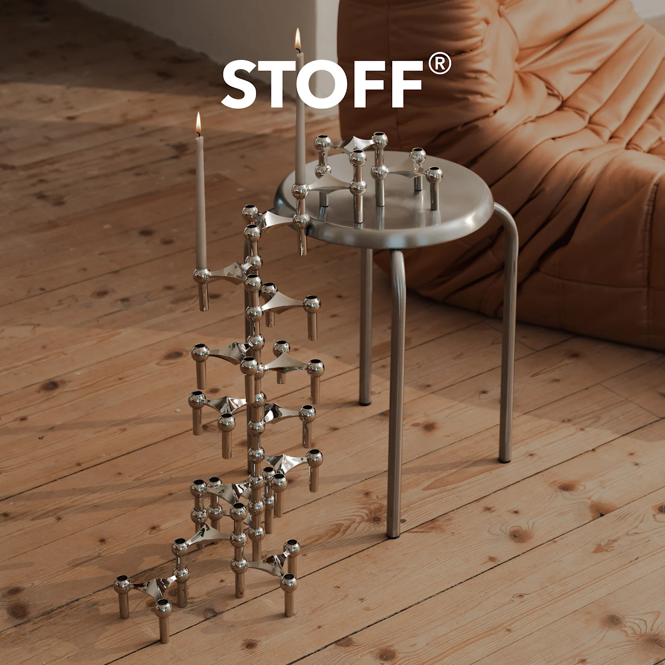 Logo STOFF sobre candelabro cromado con velas en suelo de madera, y otro en un taburete plateado.