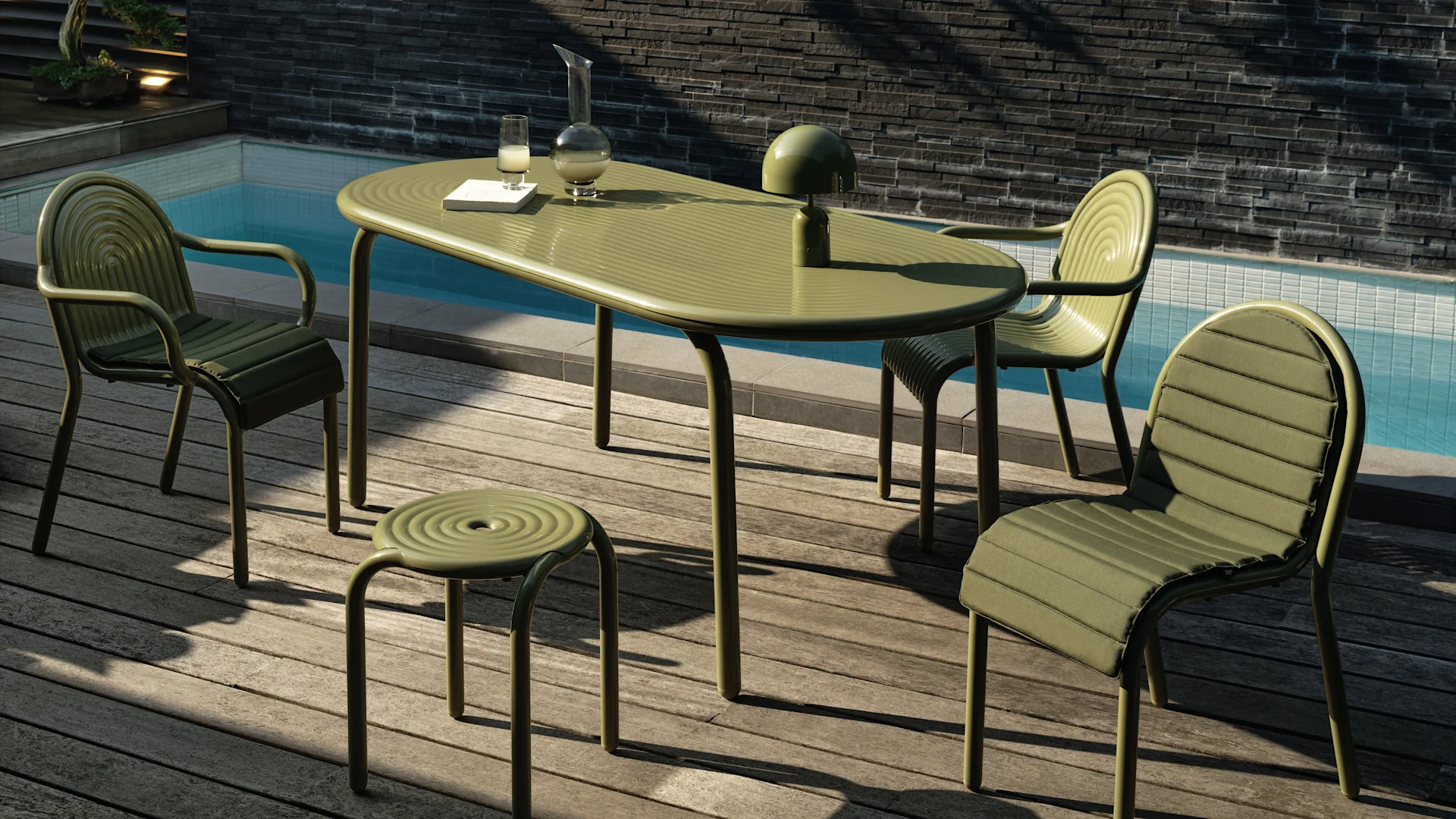 Juego de comedor exterior verde tenue con mesa ovalada, tres sillas acolchadas y un taburete en una terraza de madera junto a una piscina. Una lámpara, jarra y vaso en la mesa.
