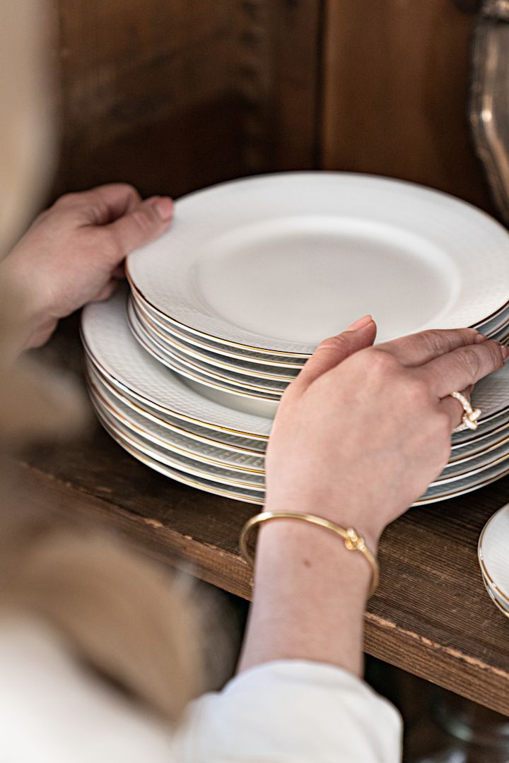 Platos blancos con un borde dorado de la serie Swedish Grace Gala, apilados en un armario.