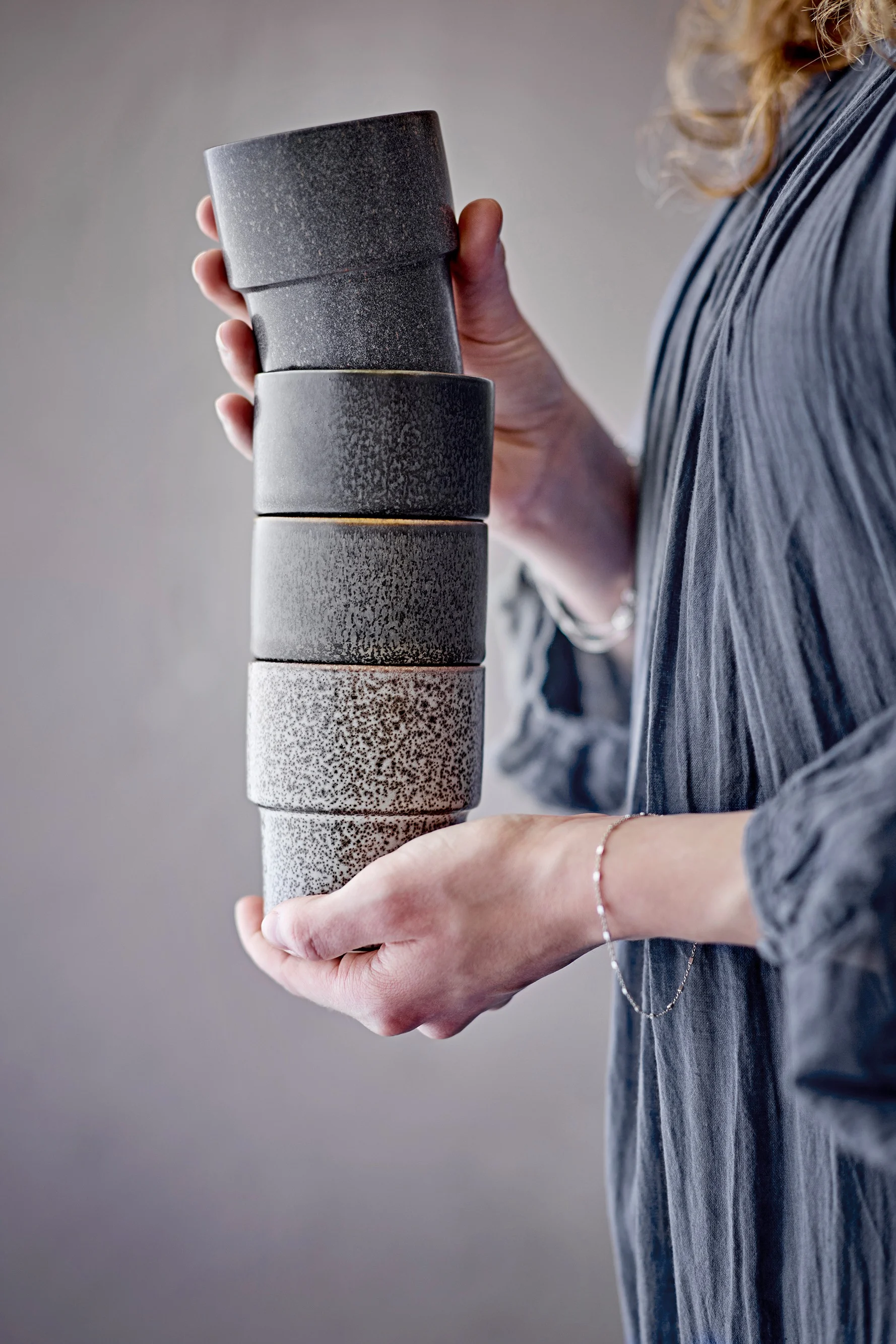 Persona sosteniendo una pila de seis tazas de cerámica moteadas, gris oscuro arriba, gris claro abajo.