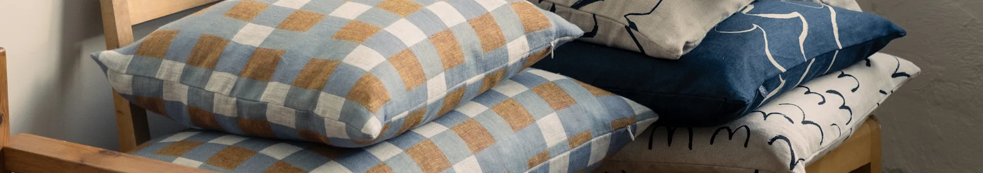 Cojines apilados en una silla de madera, con diseños a cuadros azules y marrones, y diseños abstractos azules y beige.