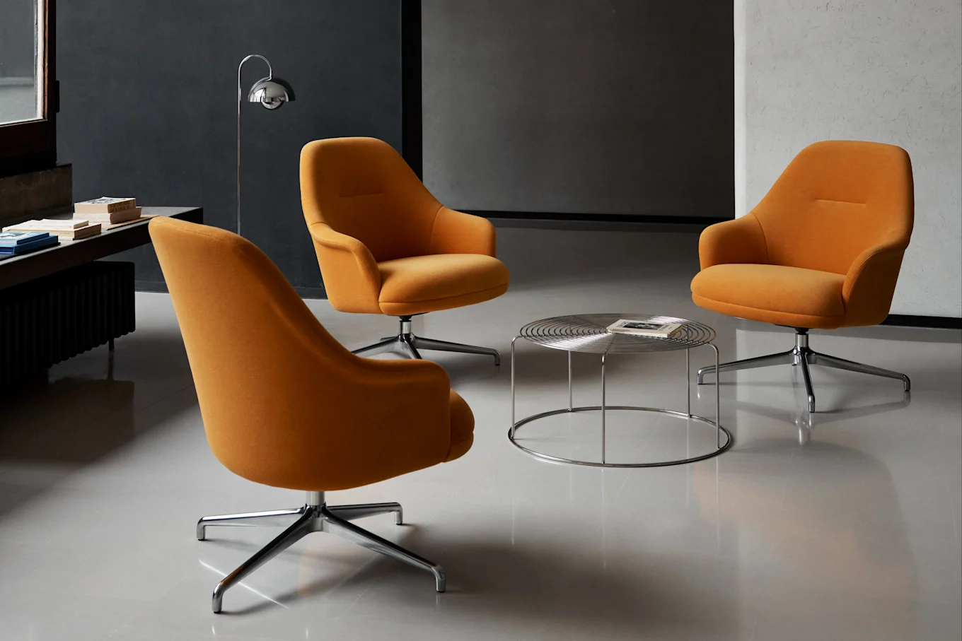 Tres sillones giratorios naranjas alrededor de una mesa de centro redonda cromada en una habitación moderna.