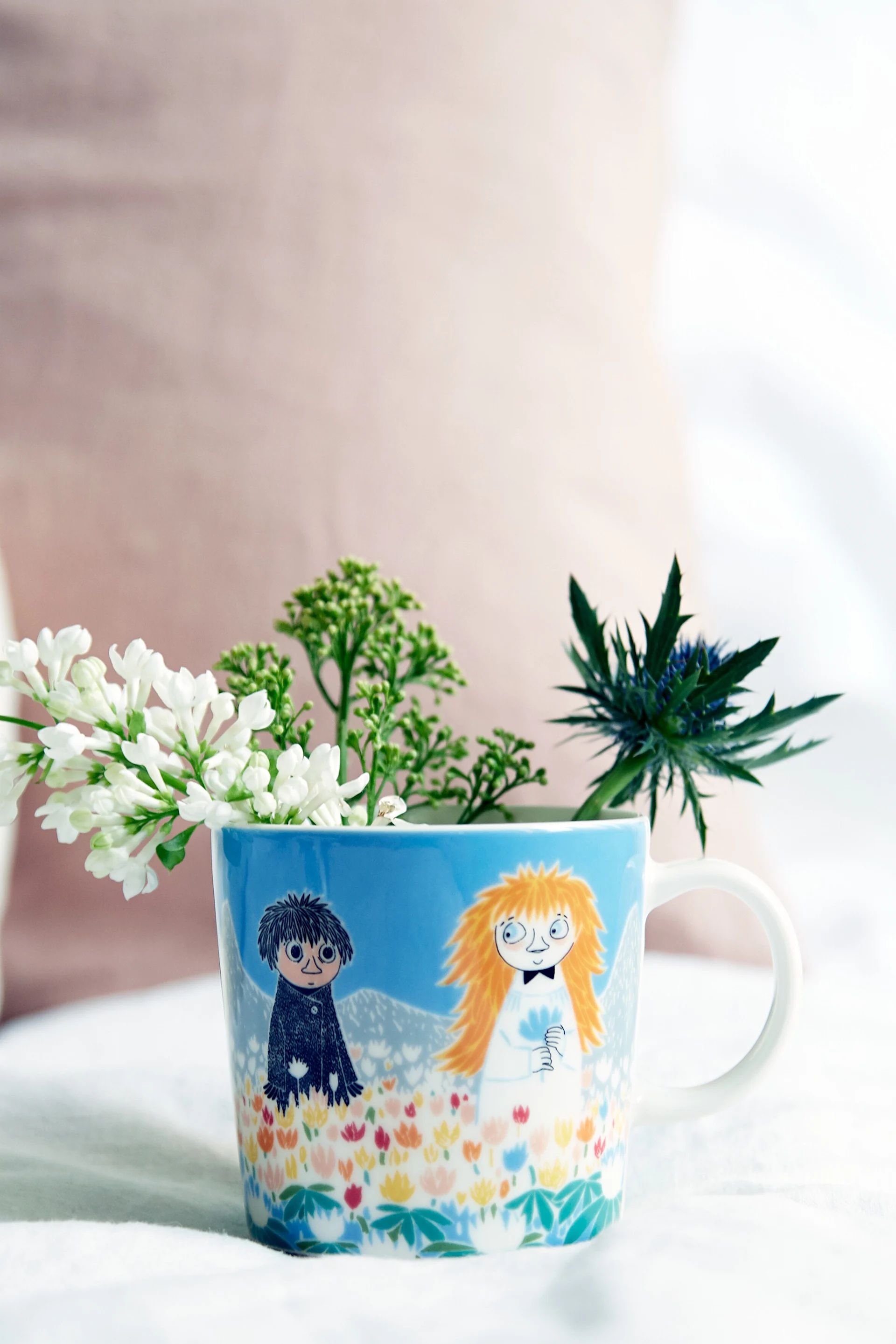 La taza Mumin "Amistad" está sobre una mesa con flores en su interior.