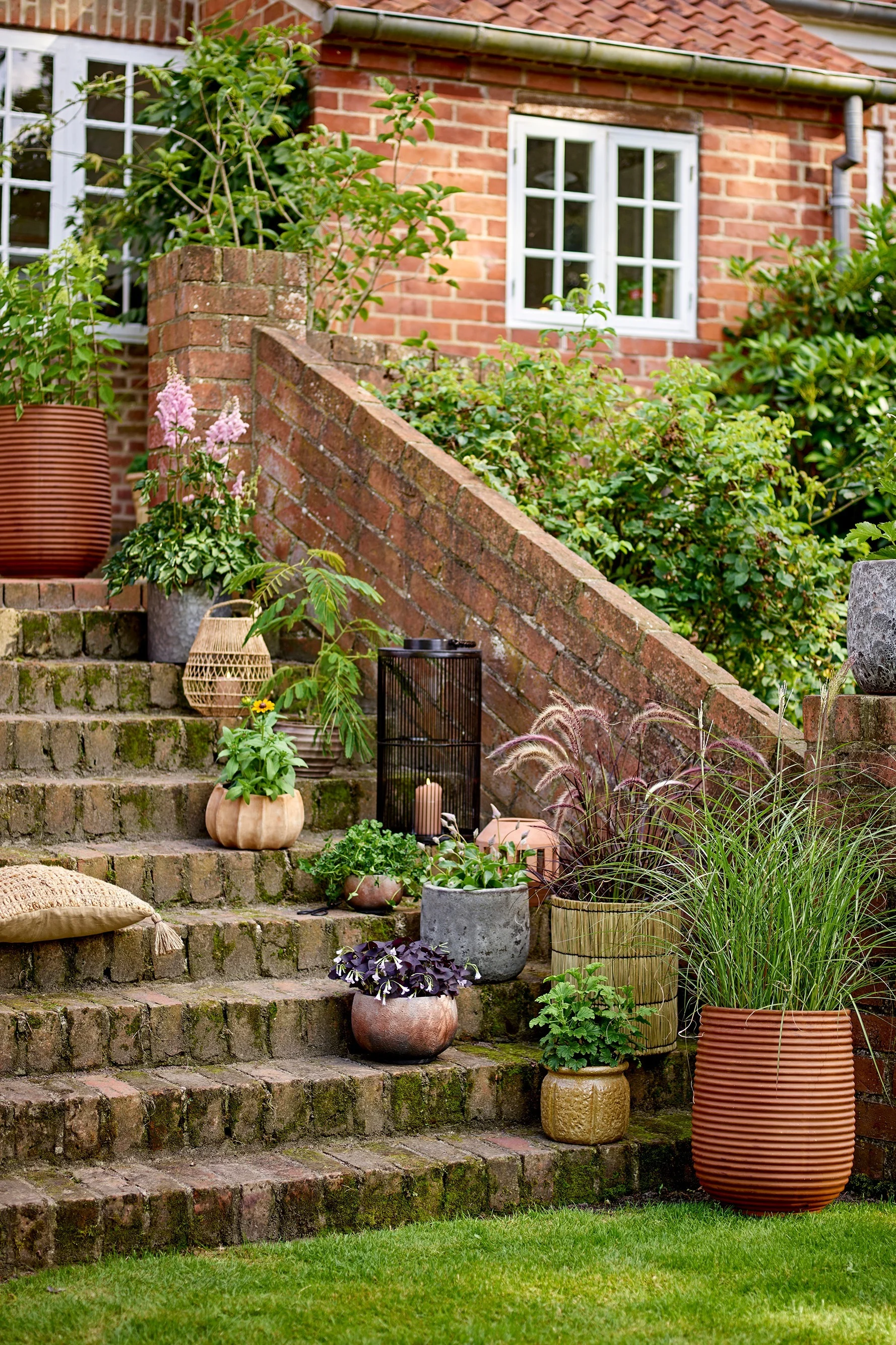 En una escalera del jardín hay varias macetas de estilo boho con plantas dentro, entre ellas la maceta Mesola de Bloomingville.